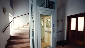 A staircase with a glass elevator door, a wooden door, and a tiled floor. - Hotel Bajt Maribor (Maribor)