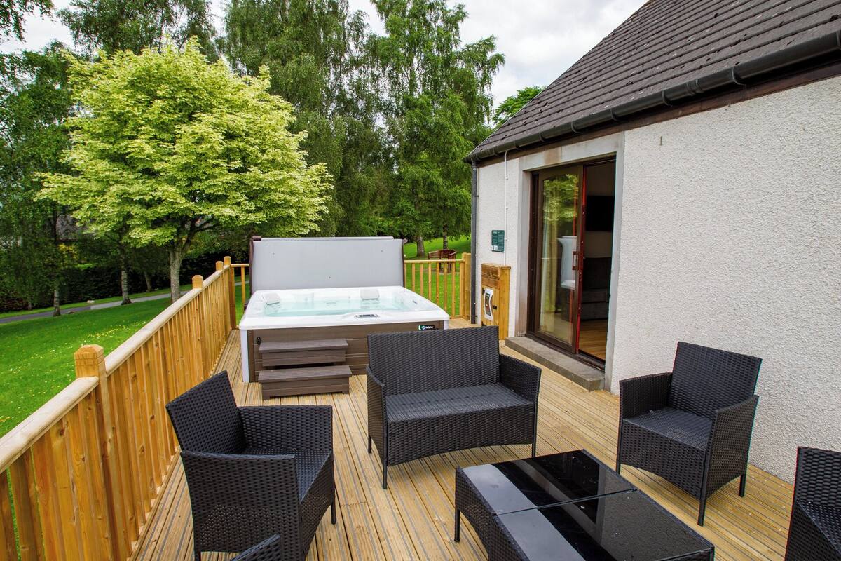 An outdoor deck with a hot tub, wicker furniture, and a wooden deck.