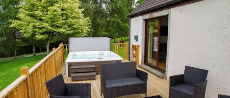Une terrasse extérieure avec un jacuzzi, des meubles en osier et une plateforme en bois.