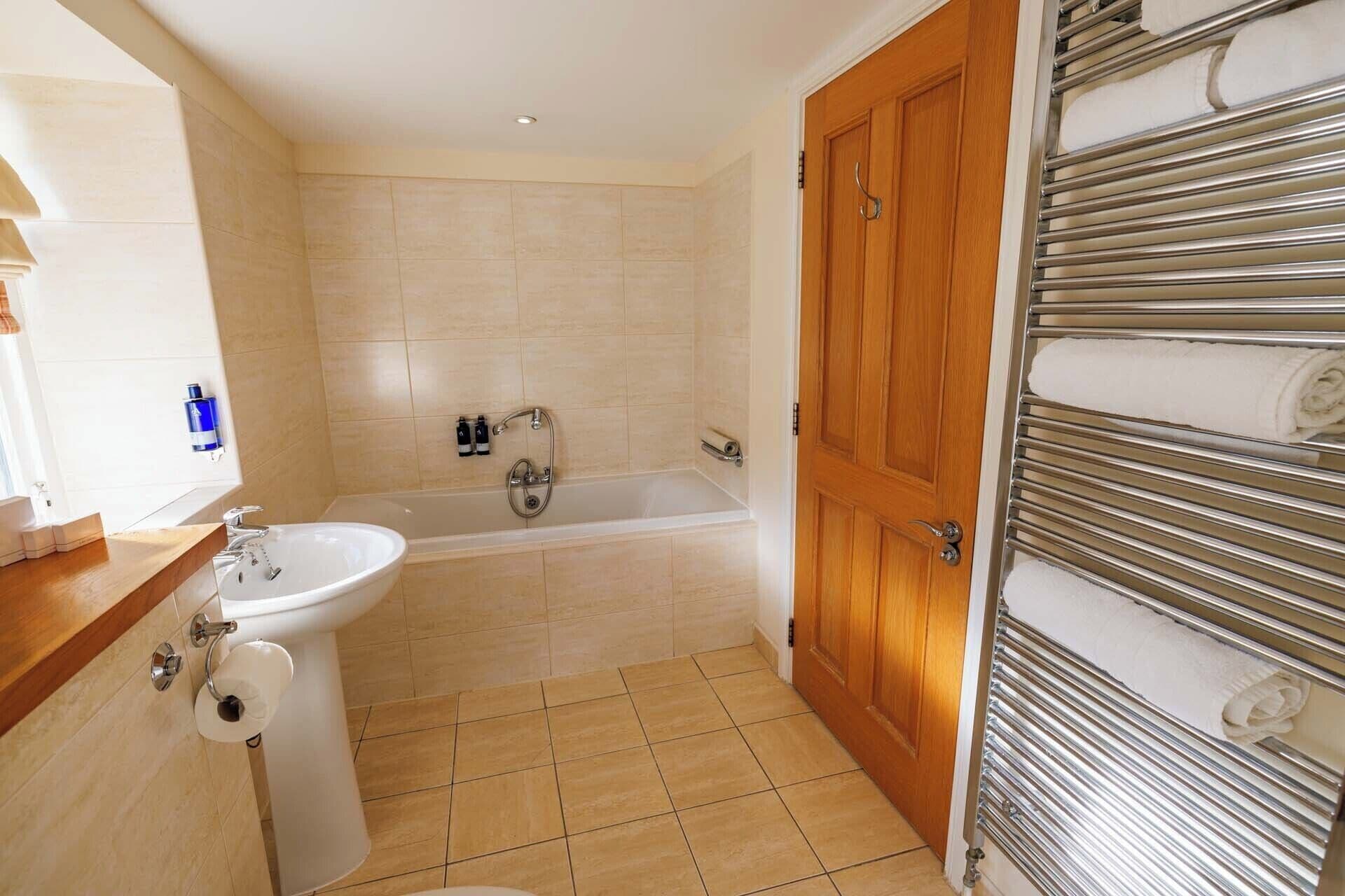 A bathroom with a bathtub, a sink, and a toilet. There is a wooden door and a towel rack with towels.