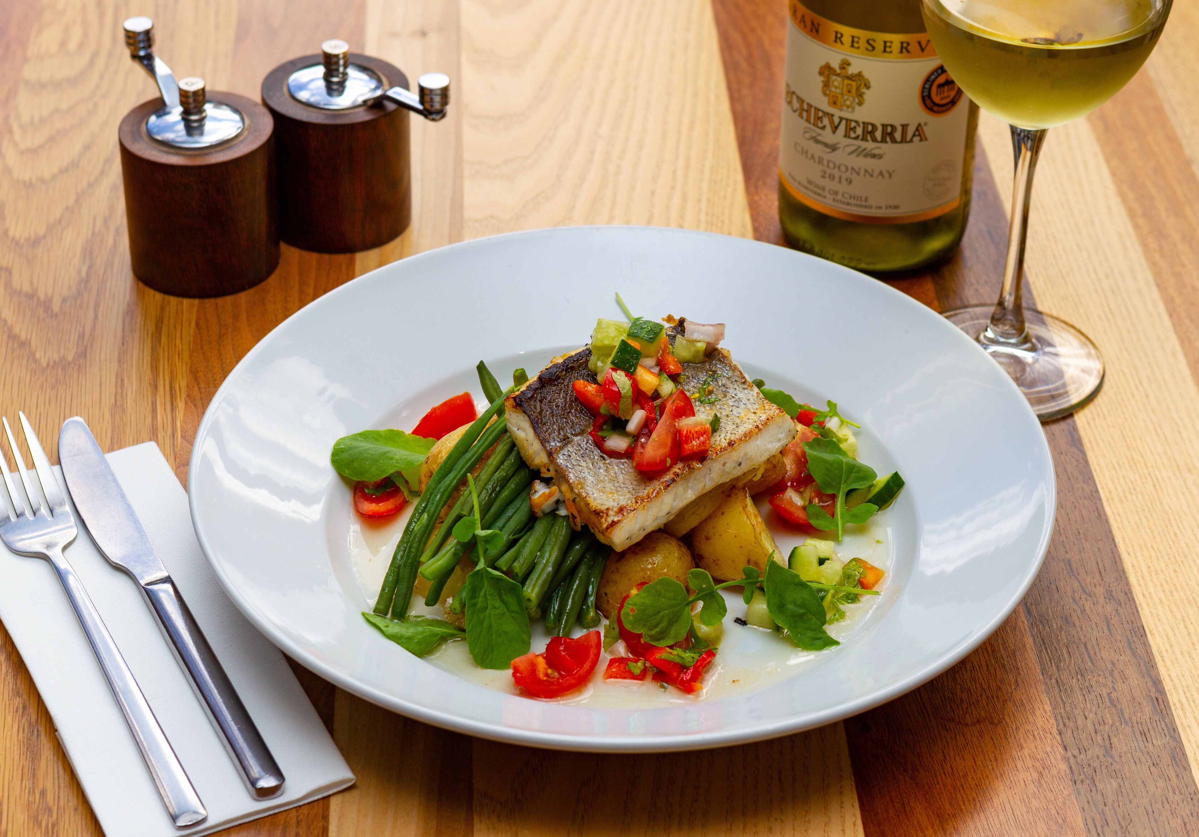 Un plato de pescado con verduras y una botella de vino sobre una mesa de madera.