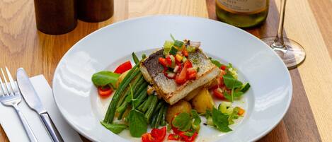 Un plato de pescado con verduras y una botella de vino sobre una mesa de madera.