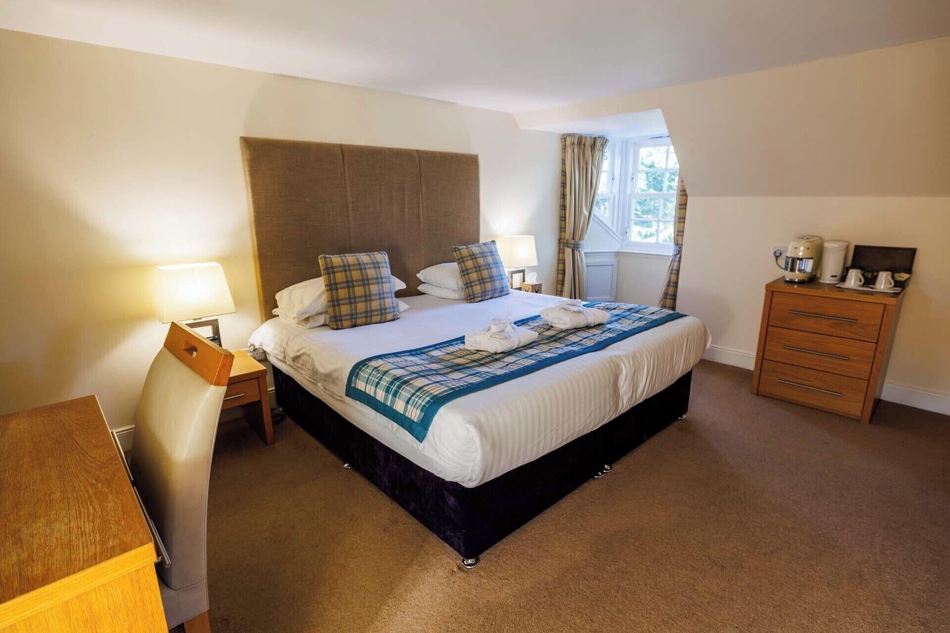A hotel room with a large bed, a wooden dresser, a desk, and a window with curtains.