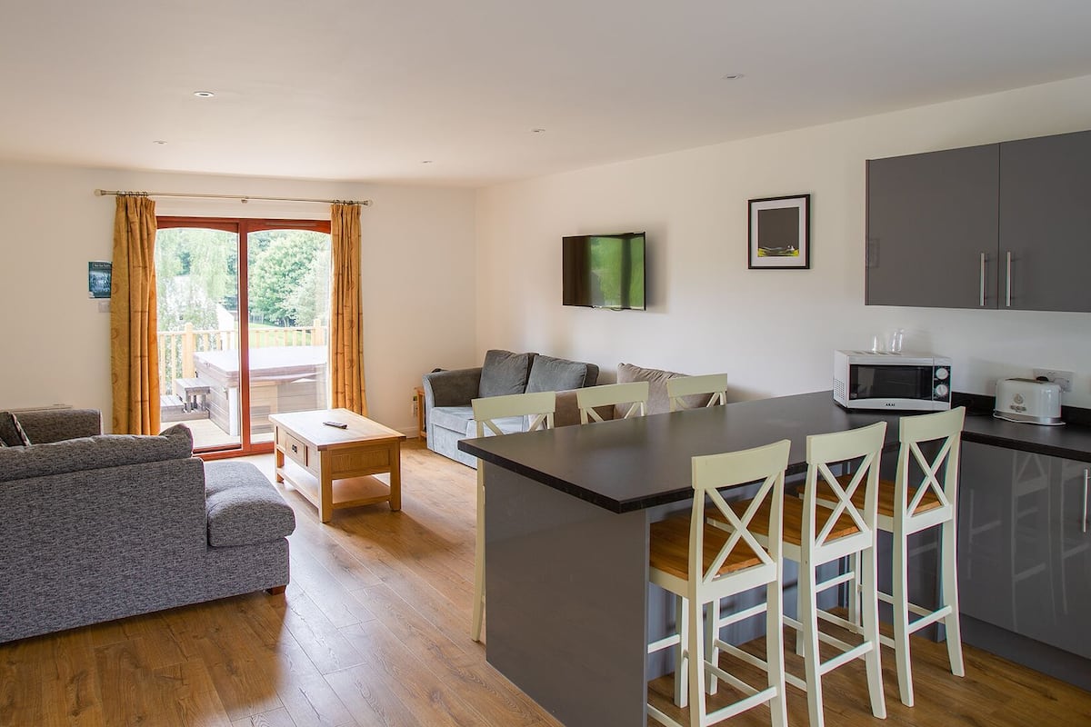 A compact living space with a sofa, a dining table, a kitchen area with a microwave and toaster, and a sliding glass door leading to an outdoor area.