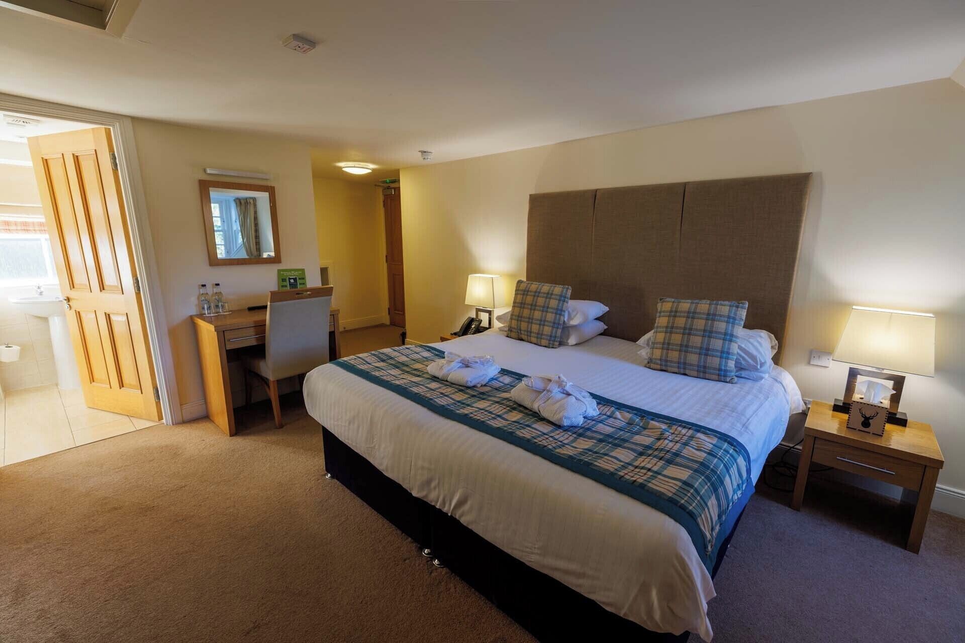 A hotel room with a large bed, bedside lamps, a desk, and a bathroom visible through an open door.