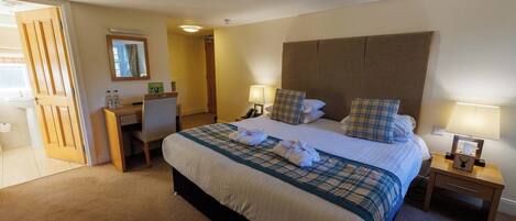 A hotel room with a large bed, bedside lamps, a desk, and a bathroom visible through an open door.