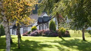 Une maison à l’extérieur blanc, avec un toit foncé et un jardin bien entretenu, agrémenté de divers arbustes et arbres.