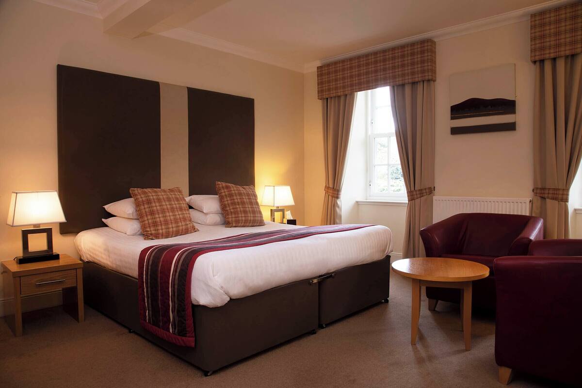A hotel room with a large bed, two bedside tables with lamps, a red armchair, and a small round table.