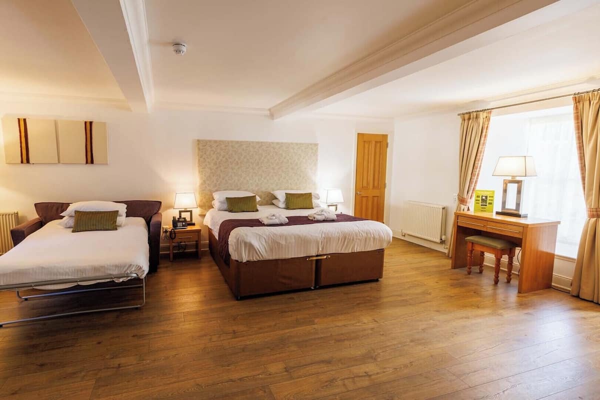 A hotel room with two beds, a desk, a chair, and a radiator.