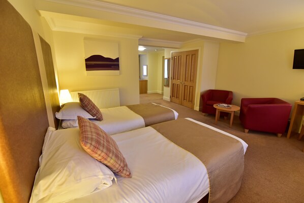 Habitación de hotel con dos camas, un sillón rojo, una mesita y un televisor.