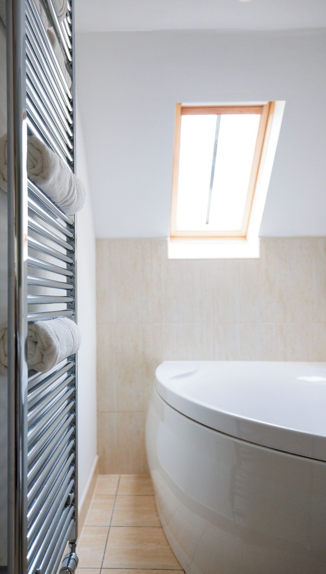 A bathroom with a bathtub, a towel rack with towels, and a skylight.