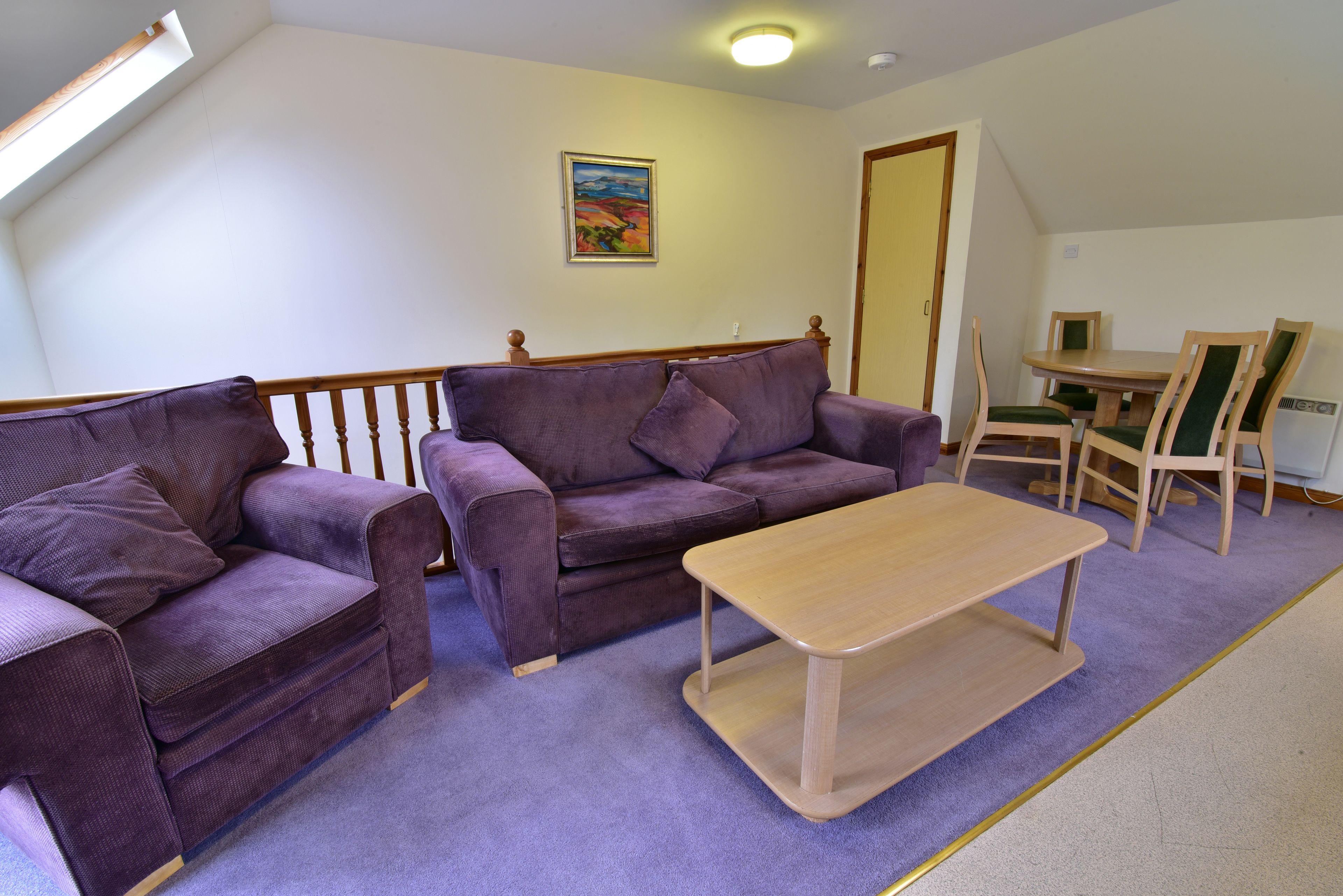 A living room with a purple sofa set, a wooden coffee table, and a dining table with chairs.
