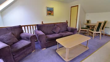 A living room with a purple sofa set, a wooden coffee table, and a dining table with chairs.