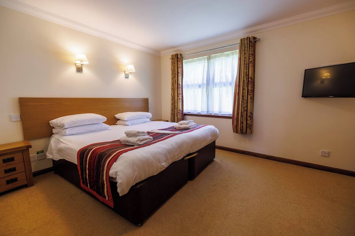 A hotel room with a bed, bedside tables, a TV, and curtains.