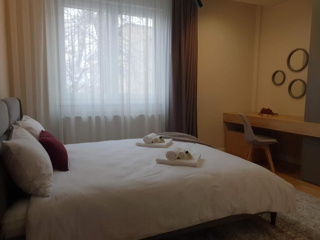 A hotel room with a large bed, a desk, and a chair. There are towels on the bed and a window with curtains.