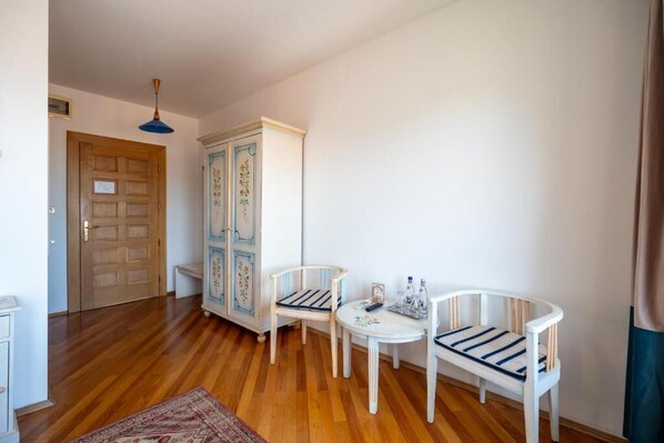 A room with wooden flooring, a white cabinet with floral designs, two white chairs with striped cushions, a small round table, and a blue hanging light fixture. - Casa Cranta Hotel (Brasov)