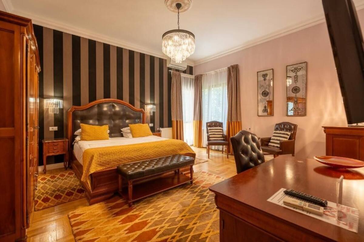 Ein Hotelzimmer mit einem großen Bett, einem Schreibtisch, einem Stuhl, einer Bank, einer Chandelüster und gestreifter Tapete.