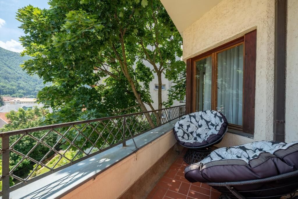 A balcony with a cushioned seating area, a metal railing, and a view of a mountainous landscape.