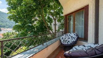 A balcony with a cushioned seating area, a metal railing, and a view of a mountainous landscape.