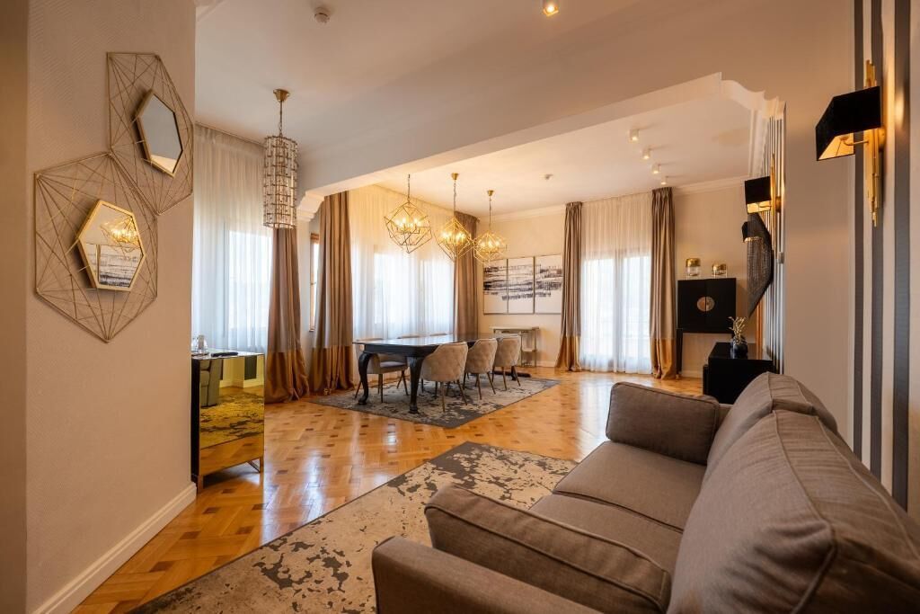 A modern living room with a sofa, a dining area with a table and chairs, and a chandelier.