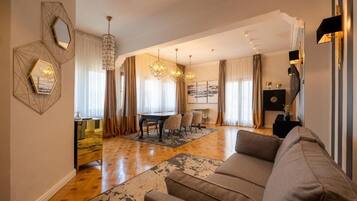 A modern living room with a sofa, a dining area with a table and chairs, and a chandelier.