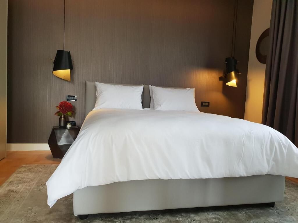 A modern bedroom with a large bed, two bedside lamps, and a nightstand with a vase.