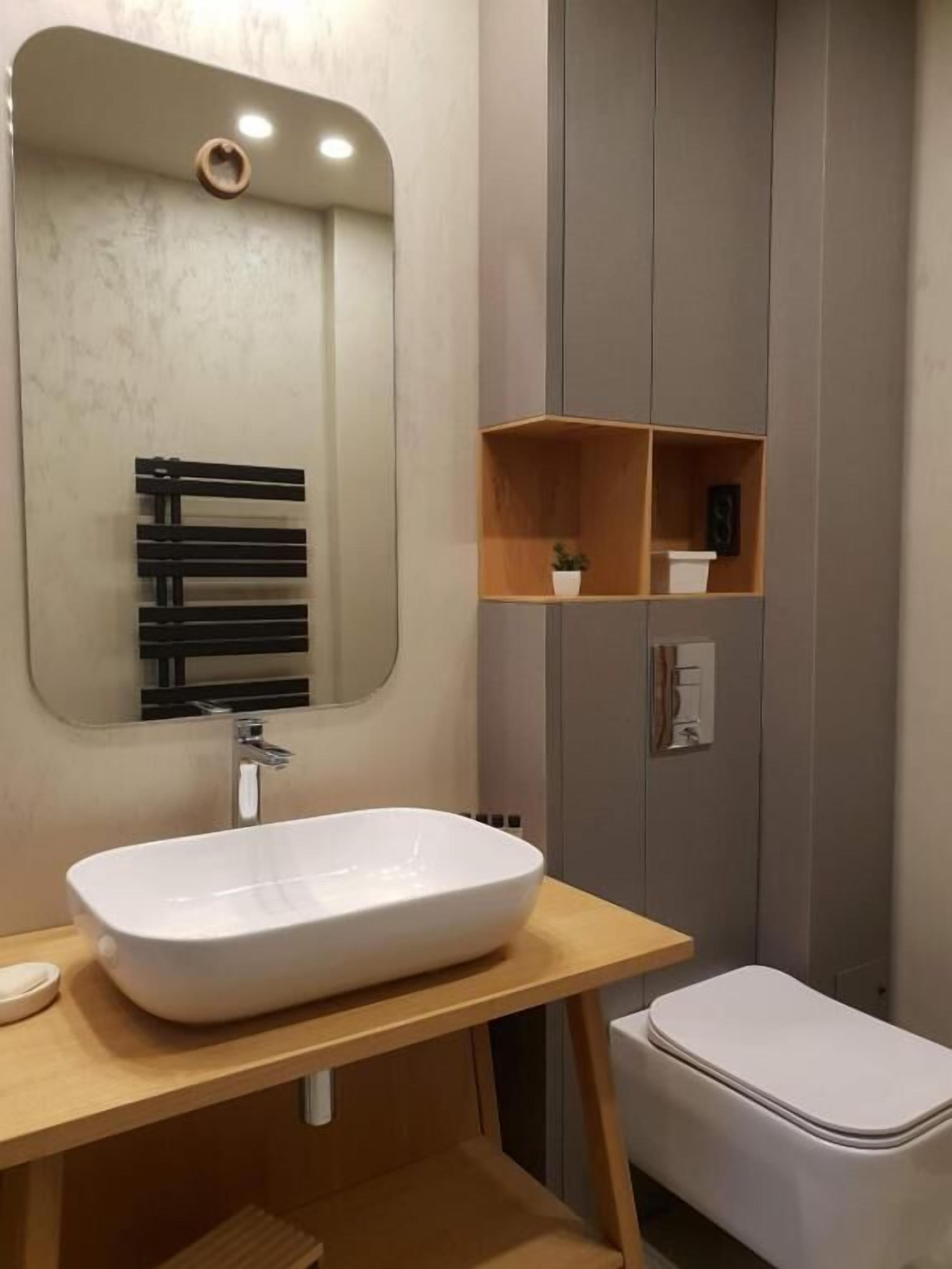 Uma casa de banho moderna com um espelho grande, uma sanita suspensa branca, um móvel de vaidade em madeira e uma sanita.