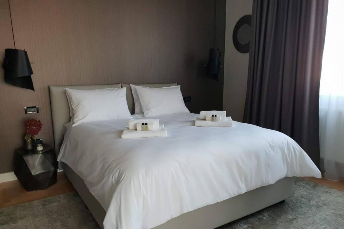 Ein modernes Hotelzimmer mit einem großen Bett, einem Nachttisch mit Lampe und Blick ins Freie.