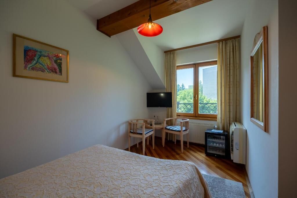 A bedroom with a bed, a desk with two chairs, a TV, a heater, and a window with curtains.