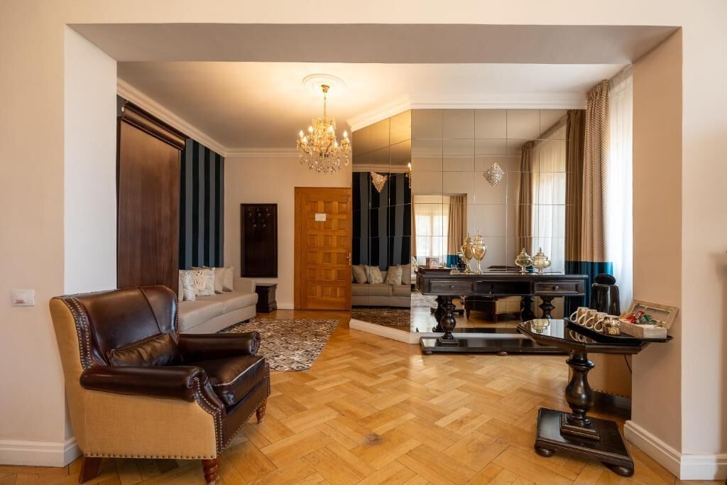 Ein geräumiges Wohnzimmer mit Ledersessel, Couchtisch aus Holz und einer Kristallleuchtre.