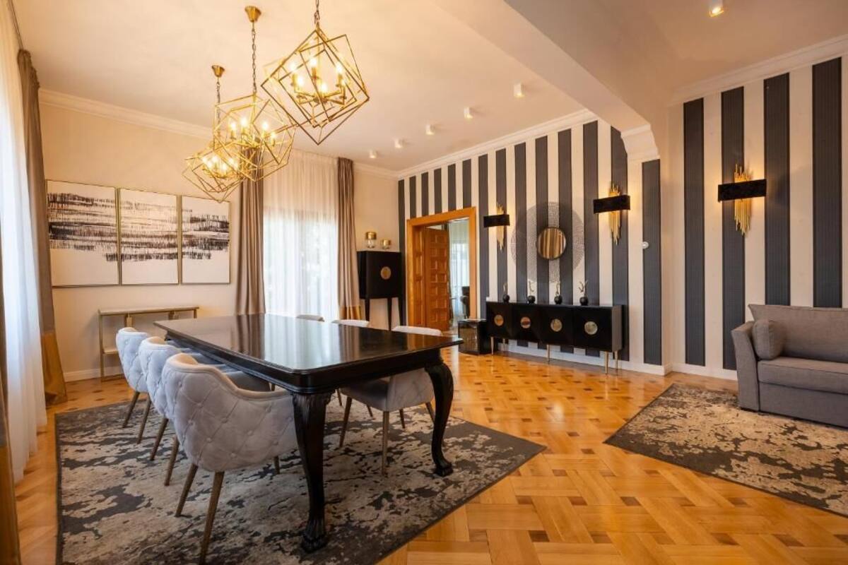 Ein modernes Wohnzimmer mit Essbereich, ausgestattet mit einem großen Holztisch, gepolsterten Sesseln und einer Kristallleuchtre.