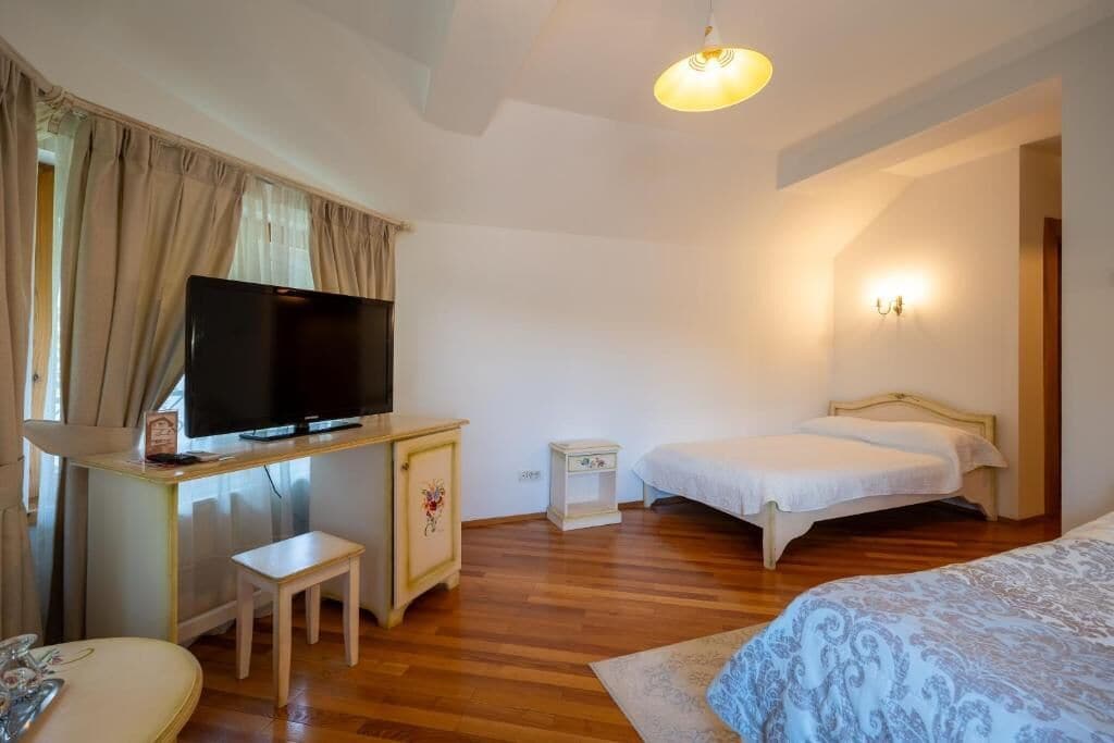 A bedroom with a bed, a TV on a desk, a small bedside table, and a nightstand.