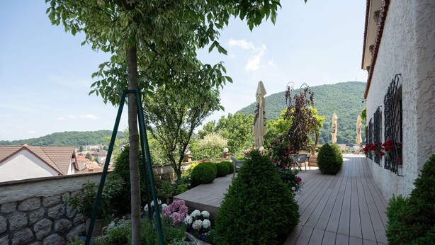 Ein Dachgarten mit Holzterrasse, Kübelpflanzen und Blick auf die Stadt und die dahinter liegenden Hügel.