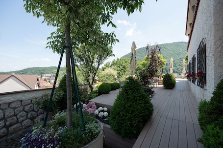 A rooftop garden with a wooden deck, potted plants, and a view of the city and hills in the background.