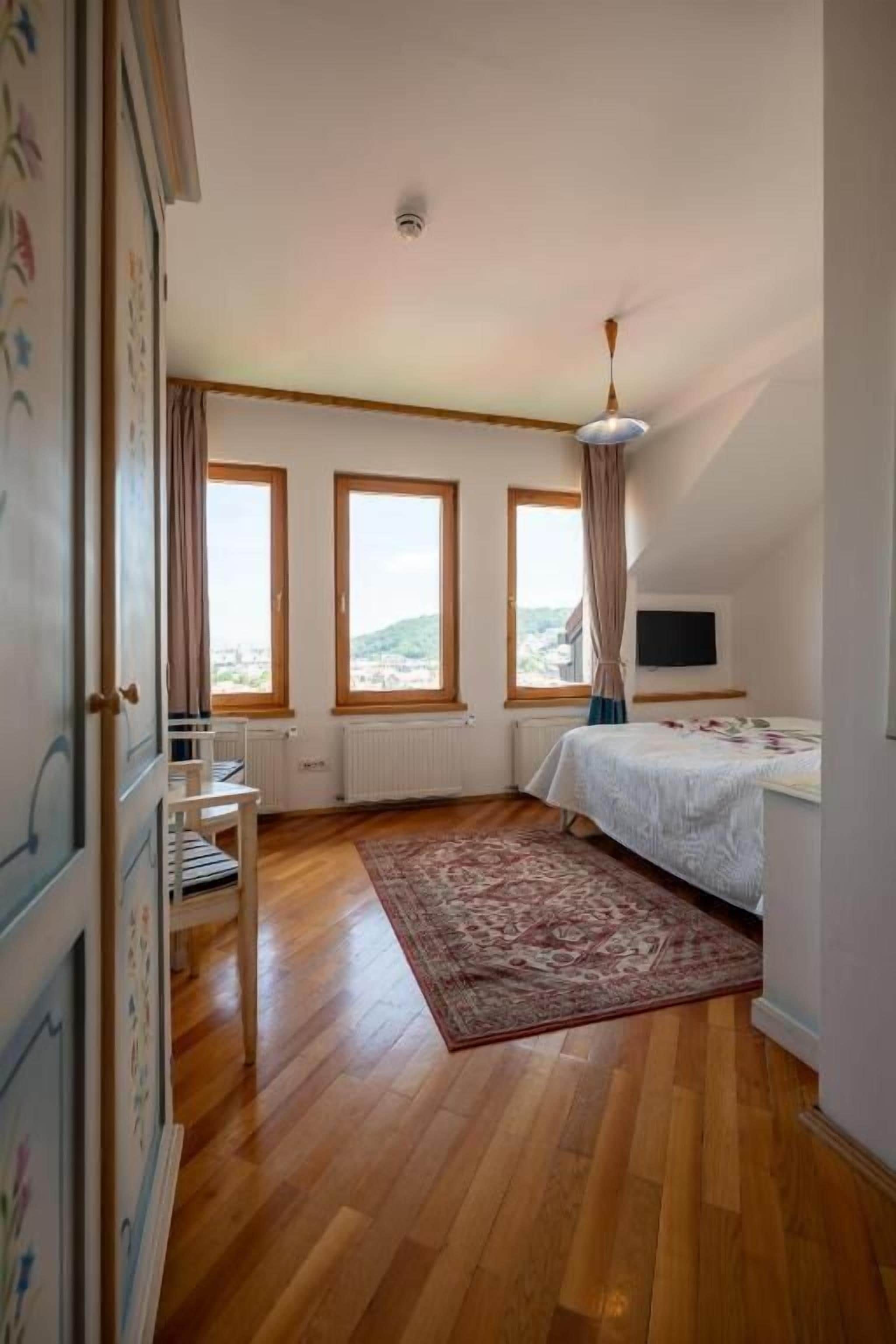 A bedroom with a bed, a TV, a ceiling fan, and large windows.