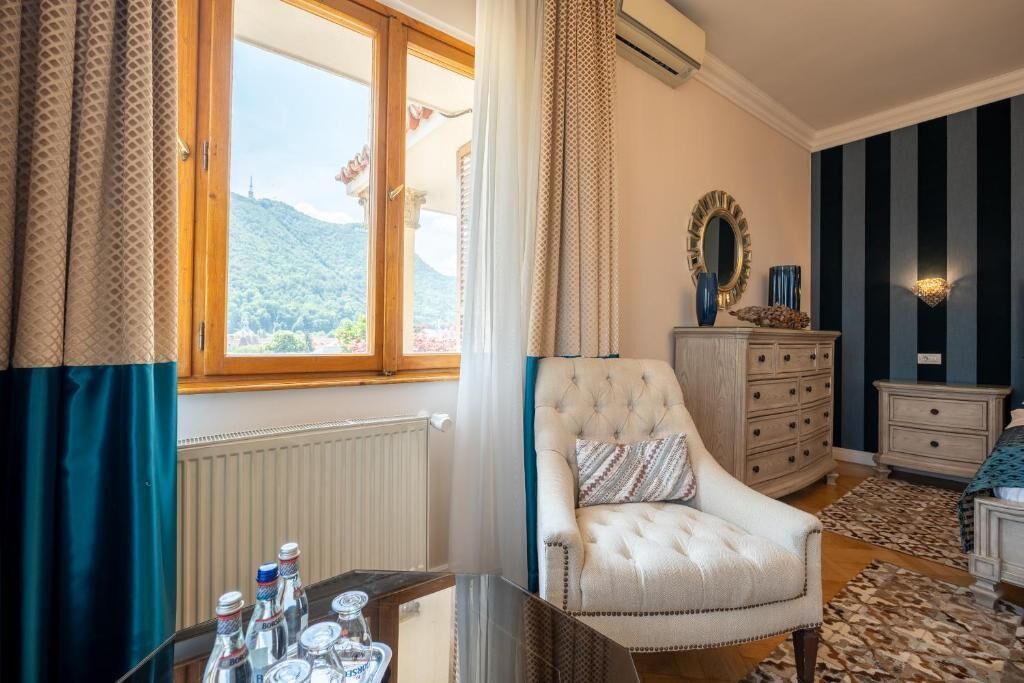 A room with a large window, a tufted armchair, a dresser, and a mirror.