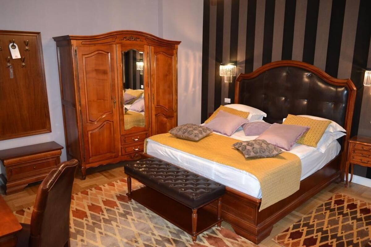 Une chambre à coucher avec un grand lit, une armoire en bois, un banc et un tapis à motifs.