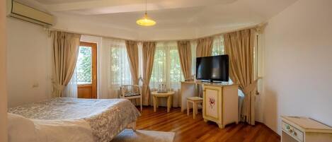 A bedroom with two beds, a desk, a chair, a television, and a window with curtains.