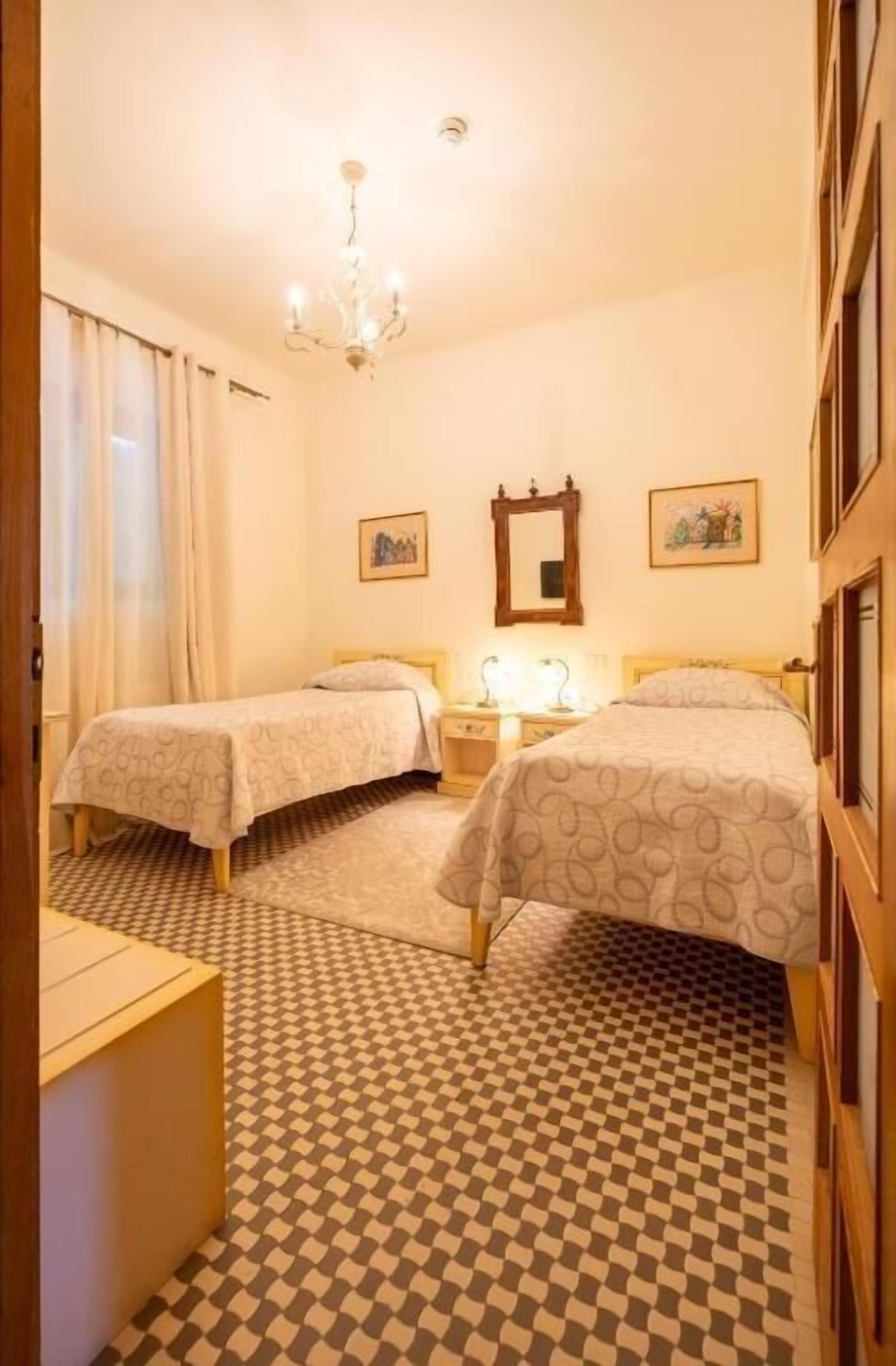 Habitación de hotel con dos camas, una araña de cristal, suelo a cuadros y un espejo en la pared.