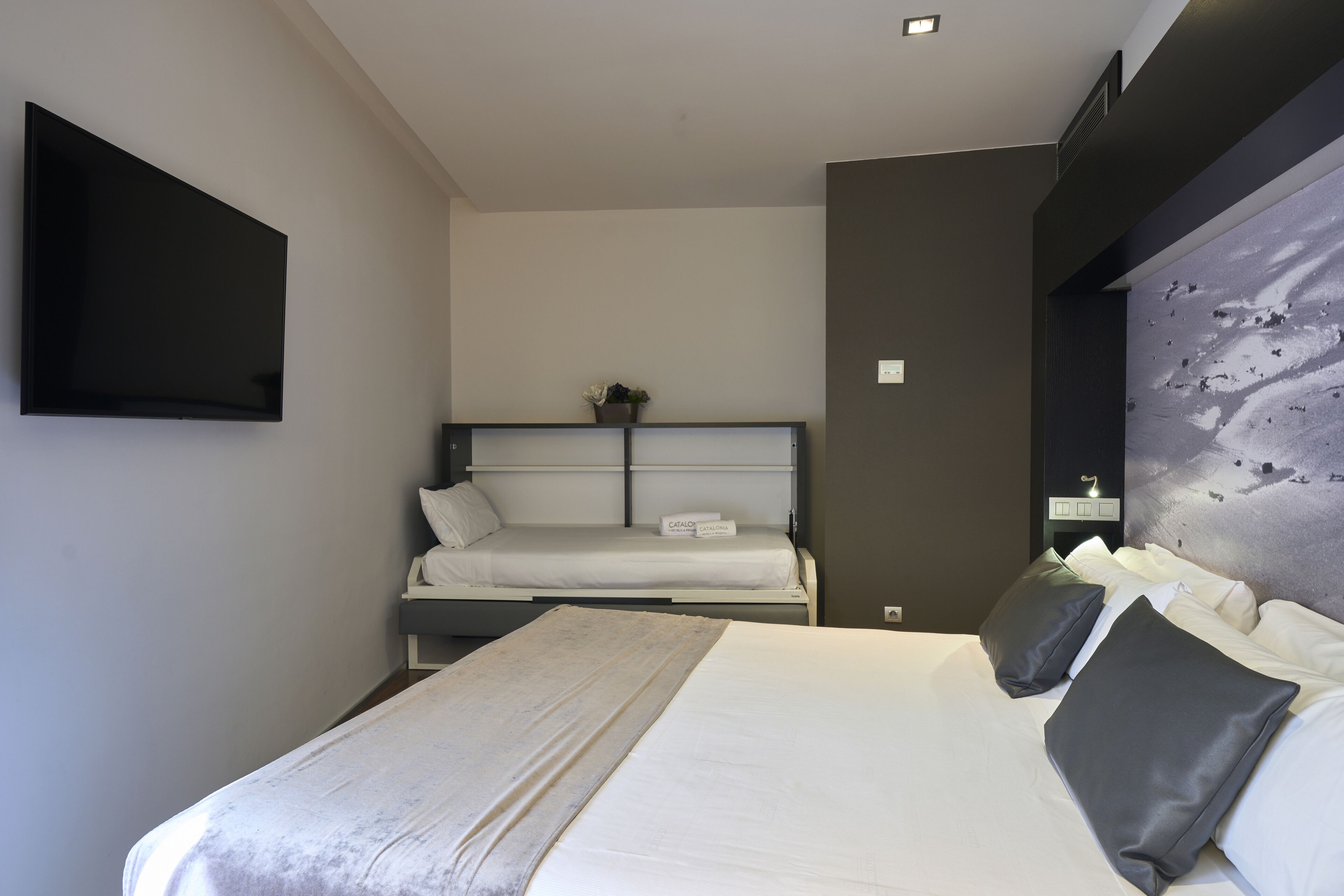 Habitació d'hotel amb un llit gran, un altre més petit, un televisor de pantalla plana penjat a la paret i una decoració mural.