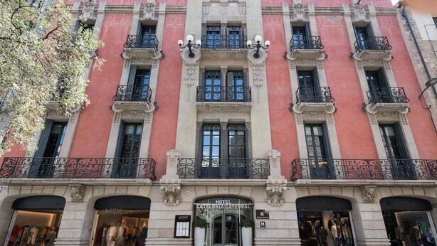 Fachada de hotel con entrada central, varios balcones y locales comerciales a ambos lados.