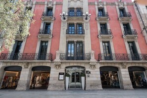Fachada de hotel con entrada central, varios balcones y locales comerciales a ambos lados.