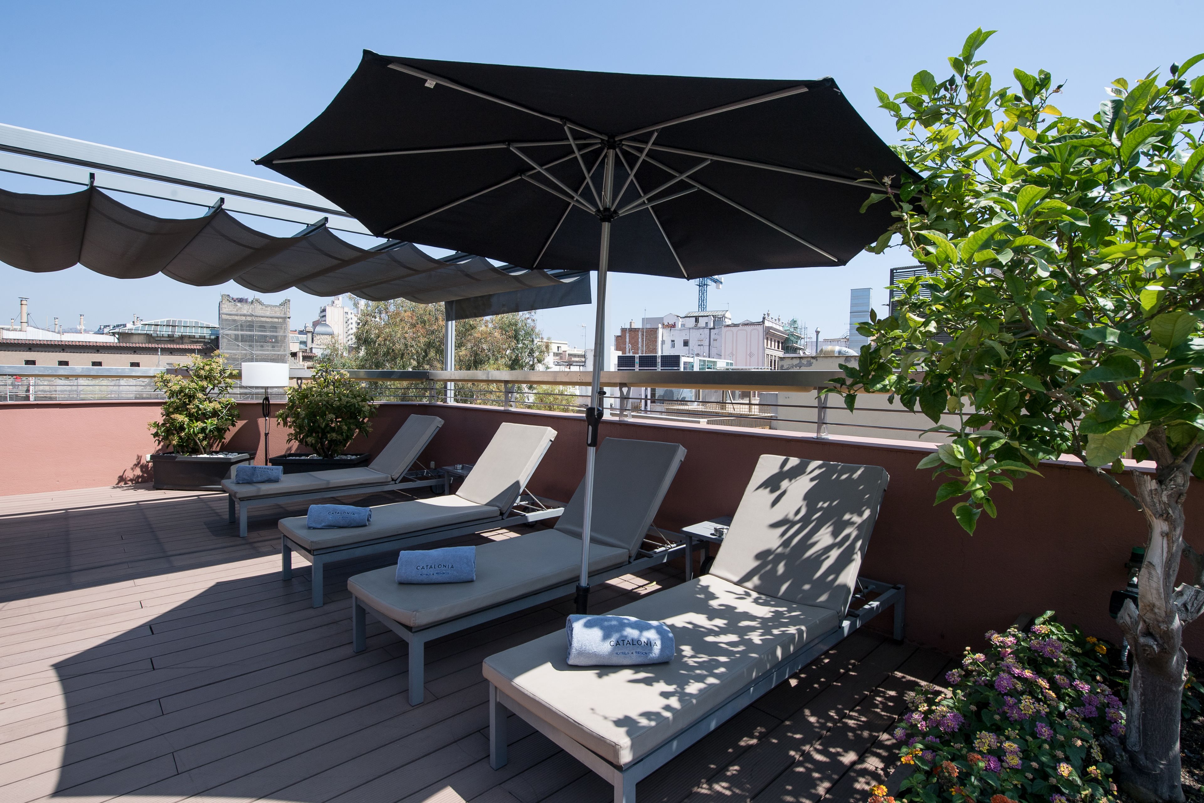 A rooftop terrace with sun loungers, a large umbrella, and potted plants.