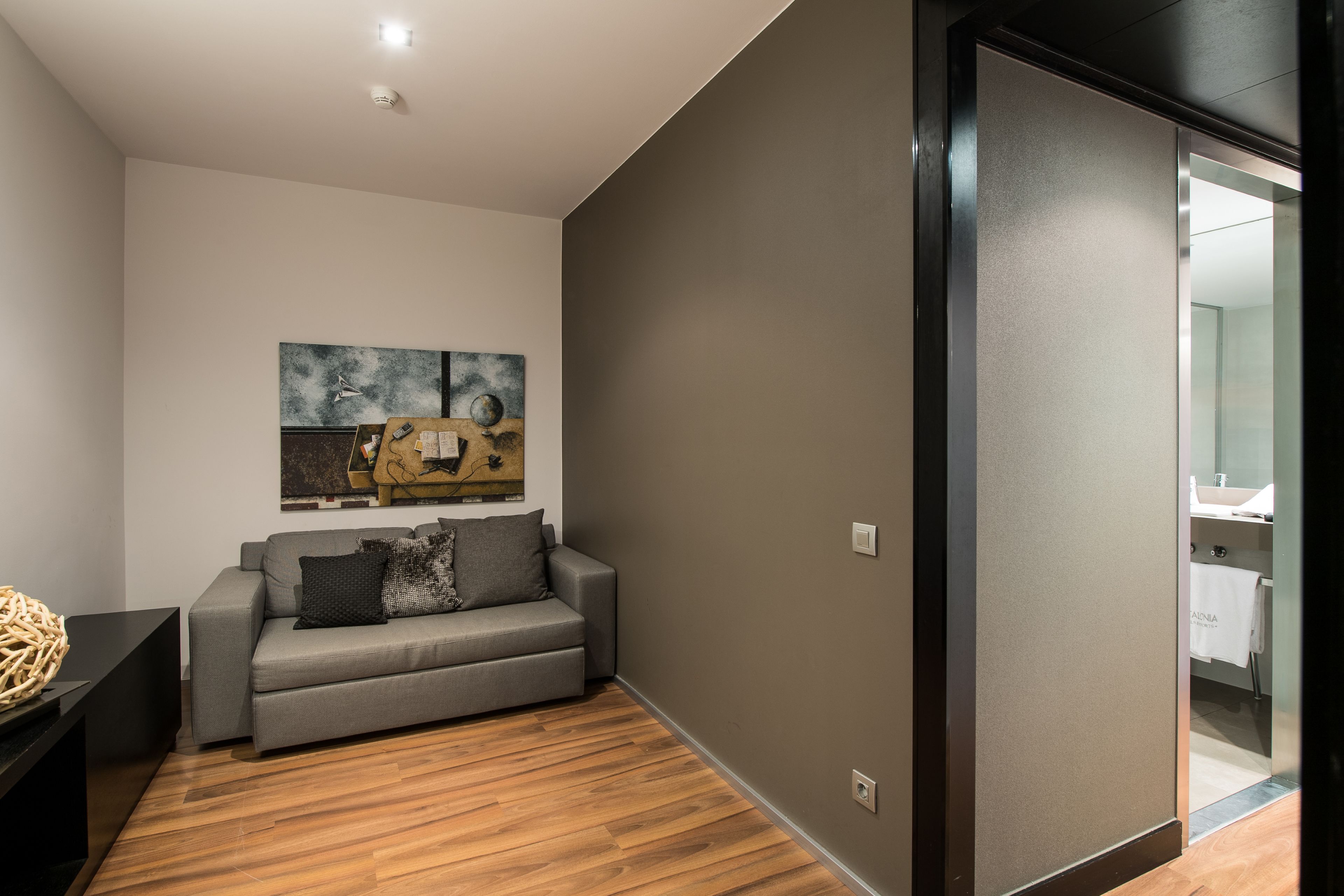 A modern living room with a grey sofa, a wooden floor, and a large abstract painting on the wall.