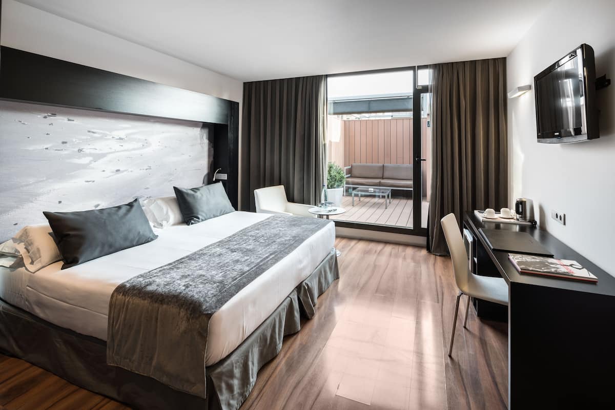 Moderni hotellihuone, jossa on suuri sänky, työpöytä, tuoli ja televisio.