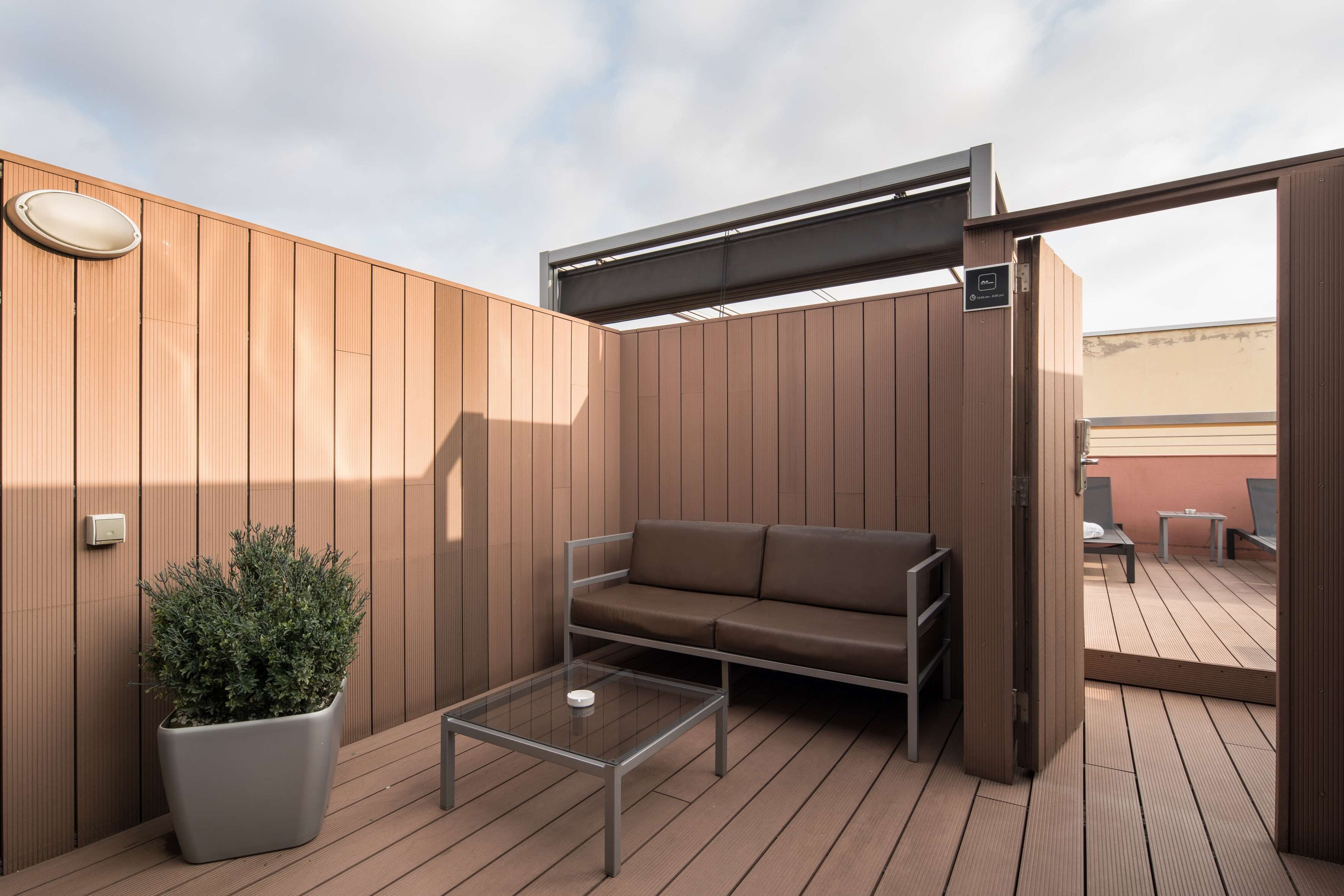 A wooden deck with a sofa, a coffee table, and a potted plant.