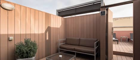 A wooden deck with a sofa, a coffee table, and a potted plant.