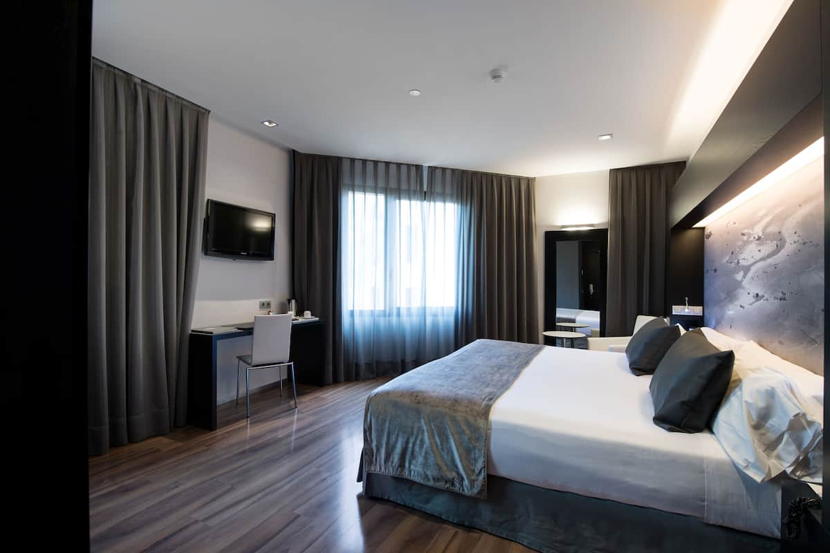 Moderni hotellihuone, jossa on suuri sänky, työpöytä ja televisio.