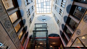 Un atrio de varios niveles con tragaluz central, detalles arquitectónicos ornamentales y un hueco para ascensor de cristal.