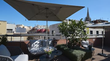 Terraza en la azotea con mobiliario exterior, incluyendo un sofá, sillas, una mesa y una sombrilla grande que proporciona sombra.